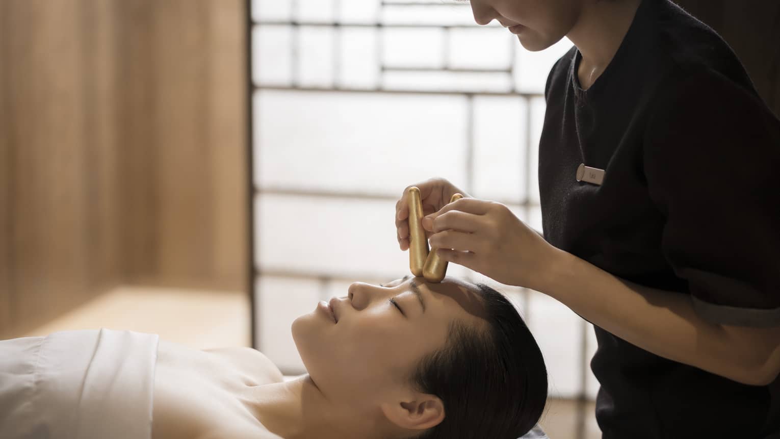 Close-up of massage therapist pressing gold acupressure batons on woman's forehead