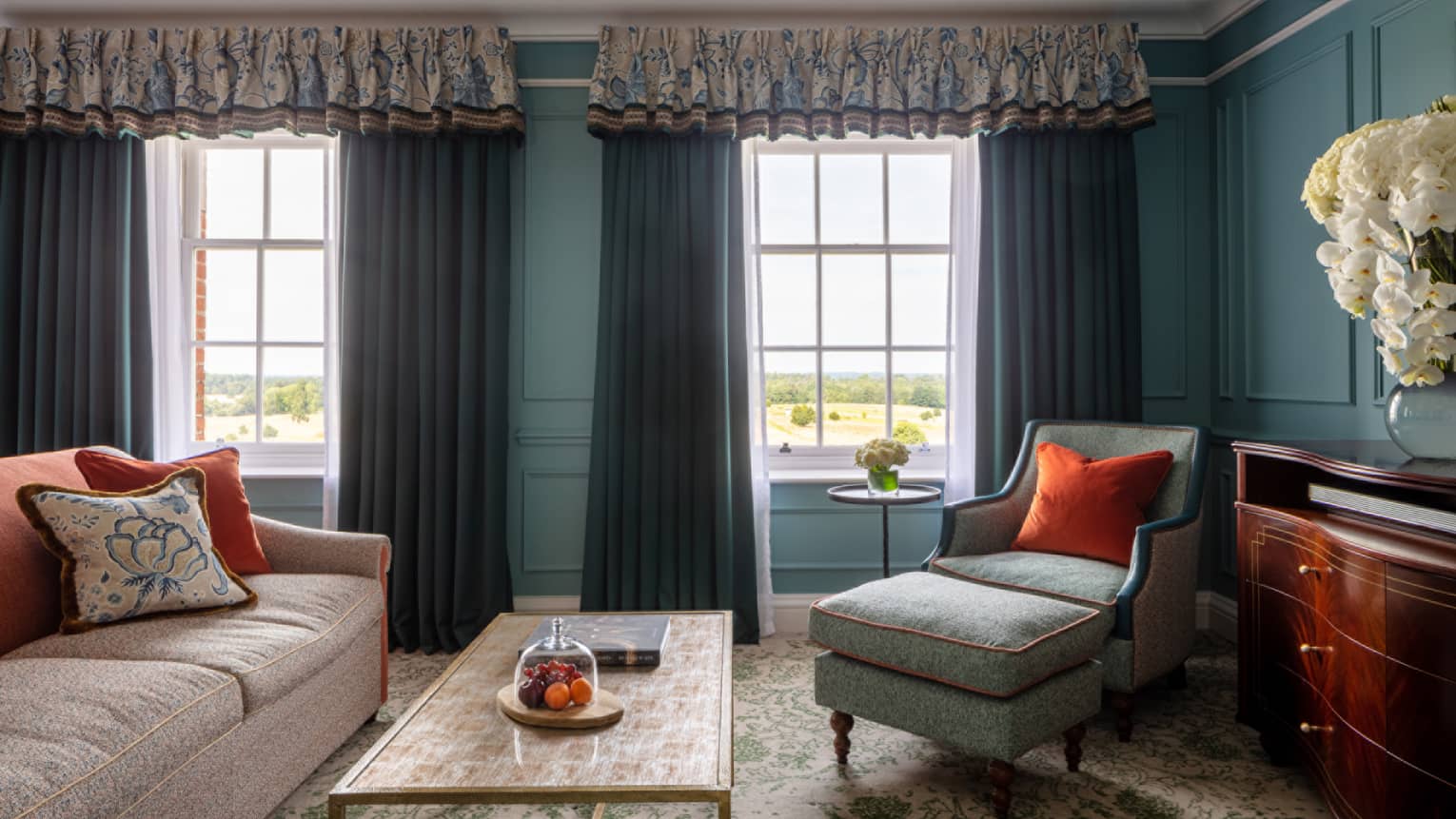 Guest room with cream couch, turquoise chaise, cherry wardrobe, twin windows with blue drapes