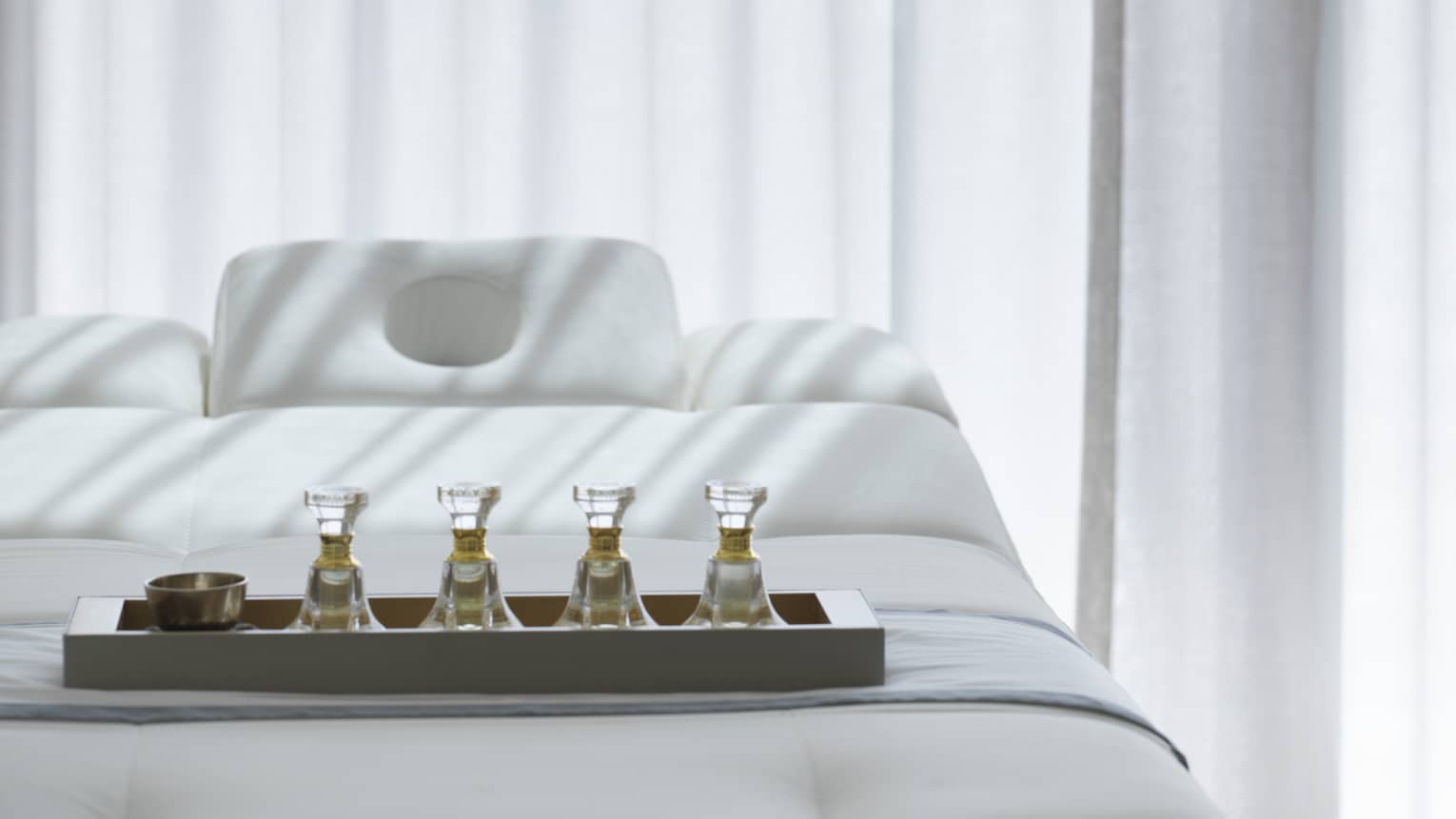 Tray with spa oils on massage treatment bed by white curtains