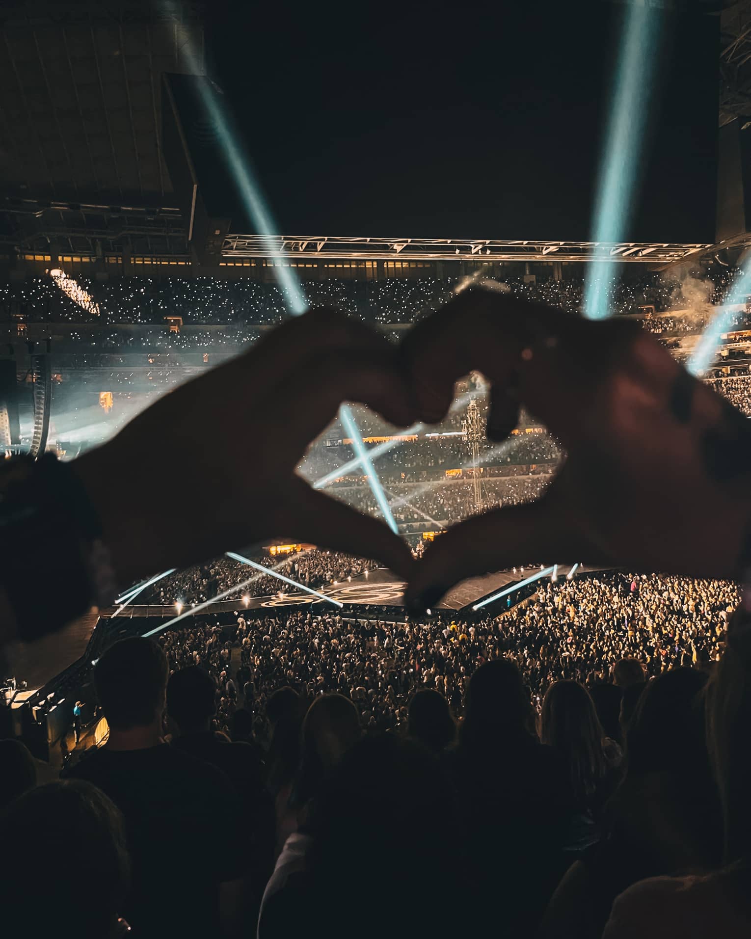 Hands held in heart shape over concert at night