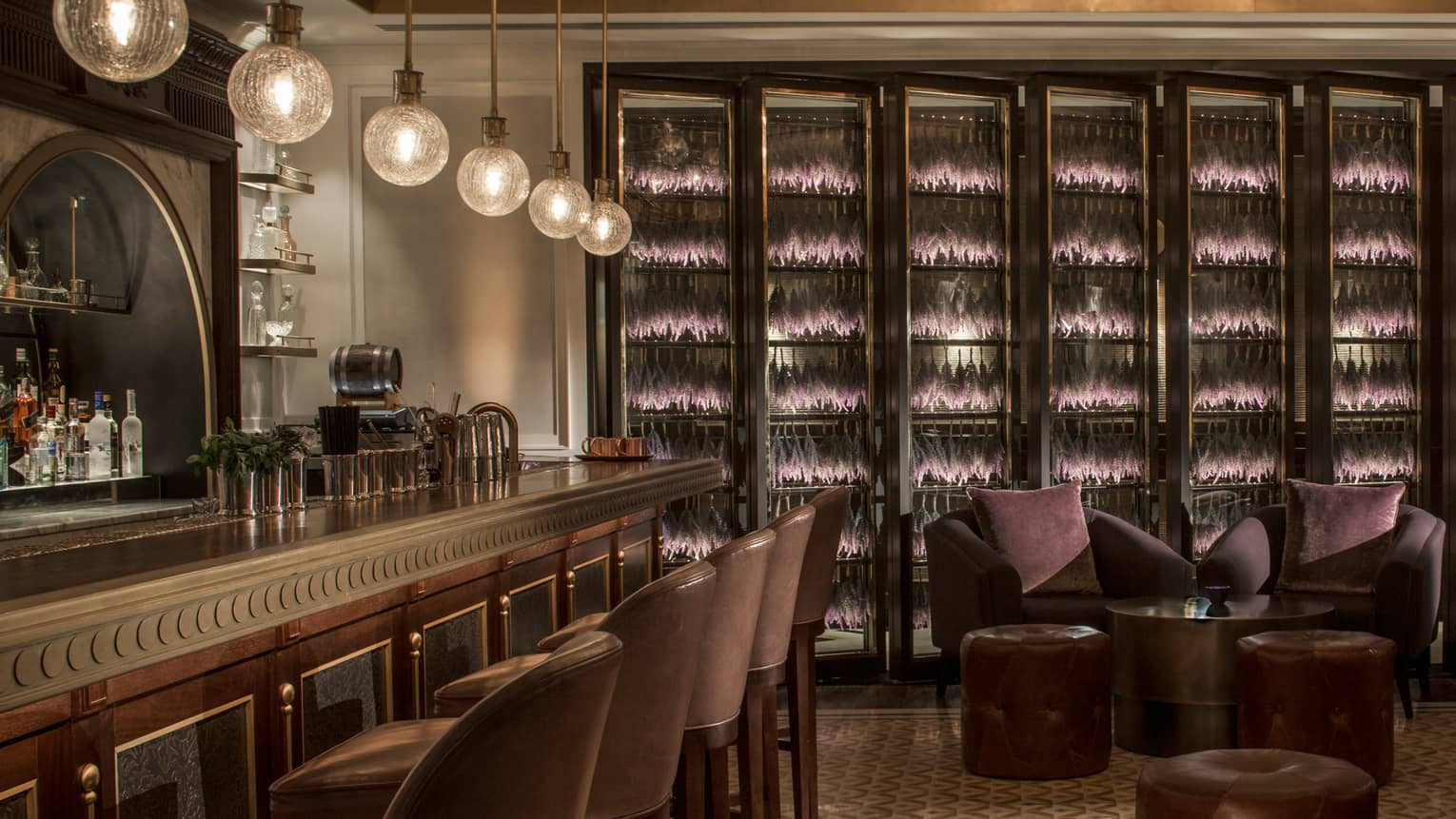 The bar at La Capitale with globe lighting, dark wood paneling, brown leather chairs and purple accents