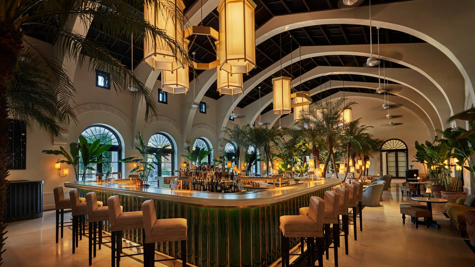Evening view of Le Sirenuse indoor Champagne bar, stools and palms lining white bar