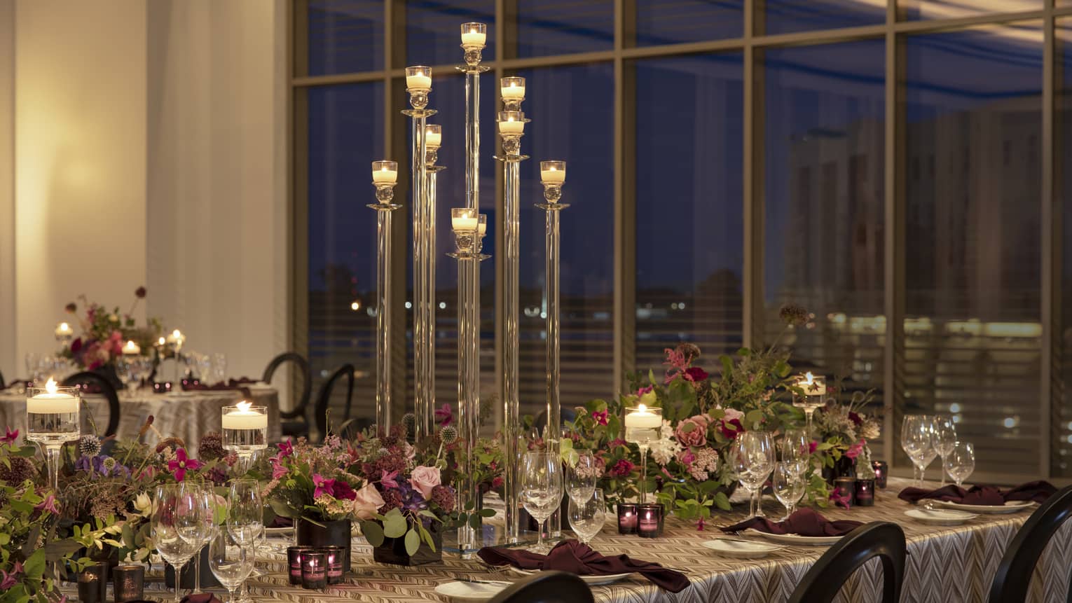 Long table in ballroom decorated with fuchsia centrepieces and greenery, tall candelabras, floor-to-ceiling window overlooking downtown New Orleans