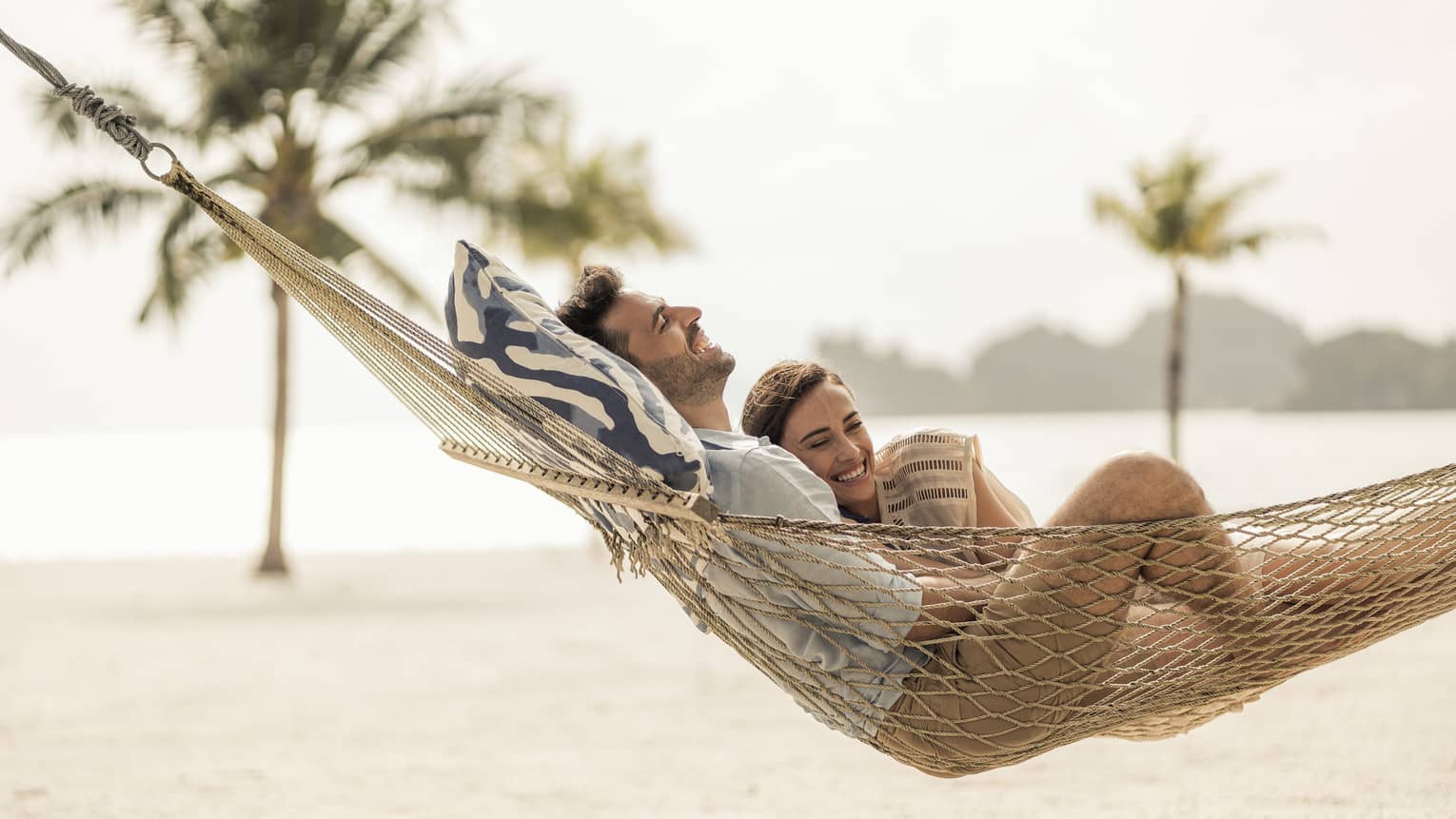 Couple lounges in hammock on sand beach