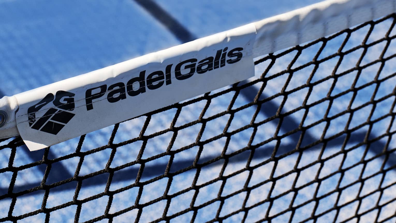 A close-up of the words, Padel Galis, and the company logo on a label of a net on a tennis court.