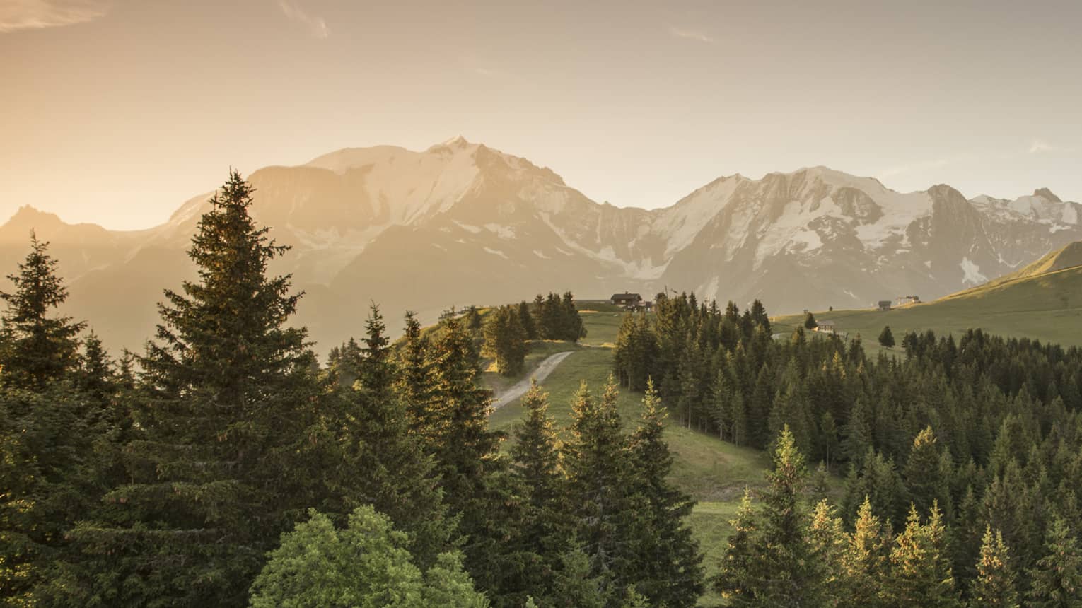 Sun sets over snow-capped mountains, green forests, trails in French Alps