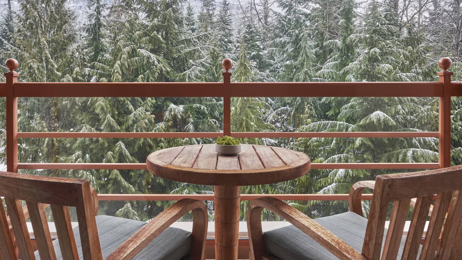 Balcony with two wooden arm chairs and a small table, overlooking the snowy forest