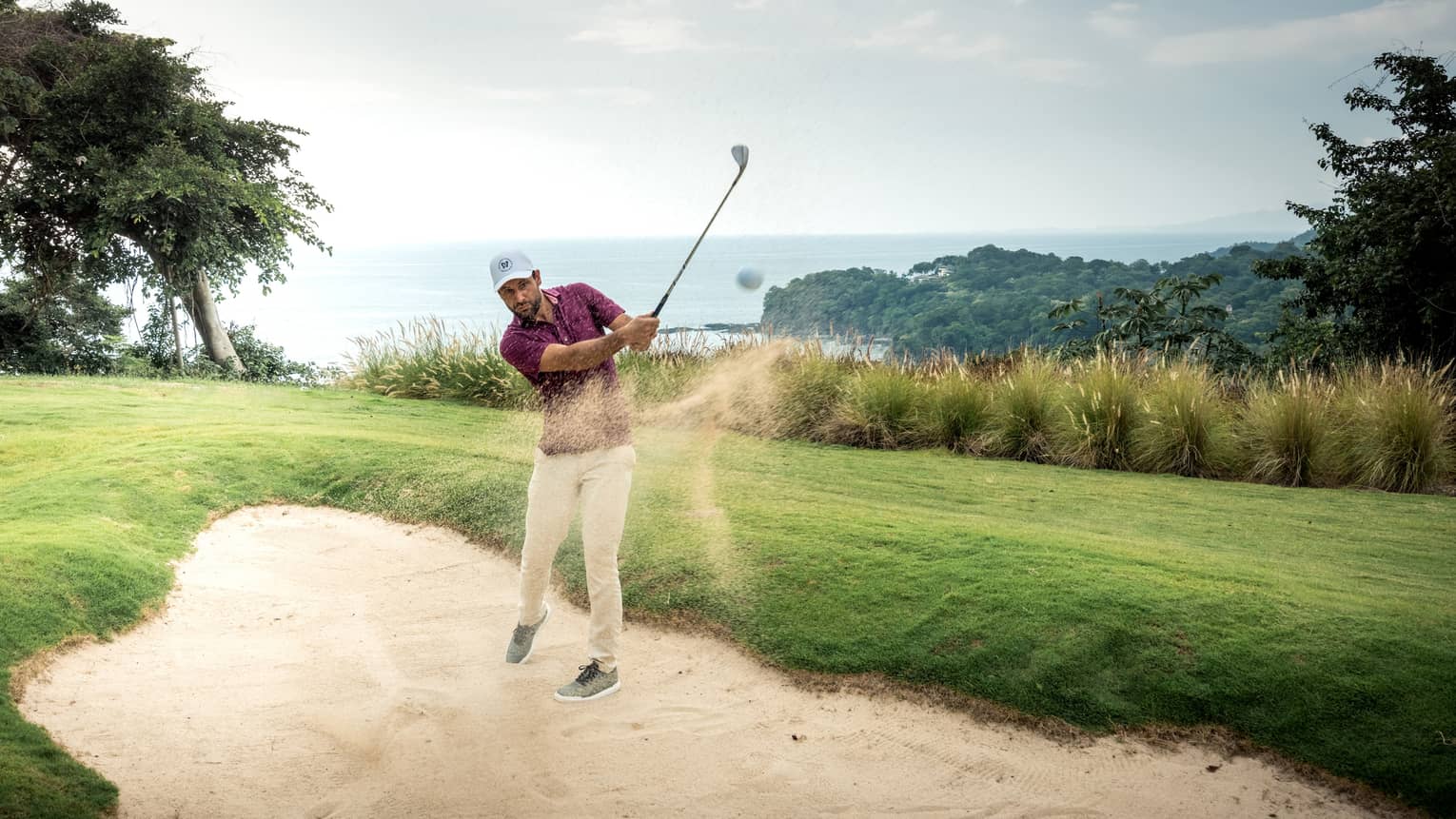 A golfer hitting a ball out of sand.