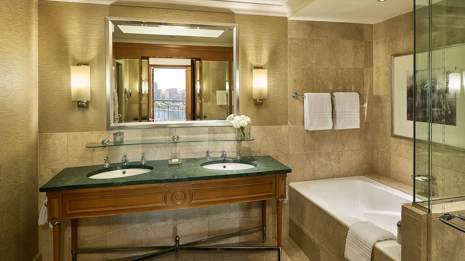 Guest room bathroom with double green granite?topped vanity, deep soaking tub,  mirror flanked by lighted wall sconces, glass shower