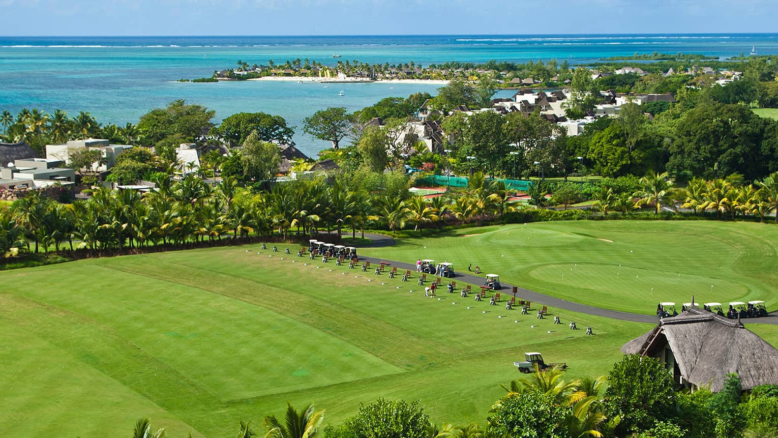 Looking down over large green lawn with rows of golf carts, trees and ocean