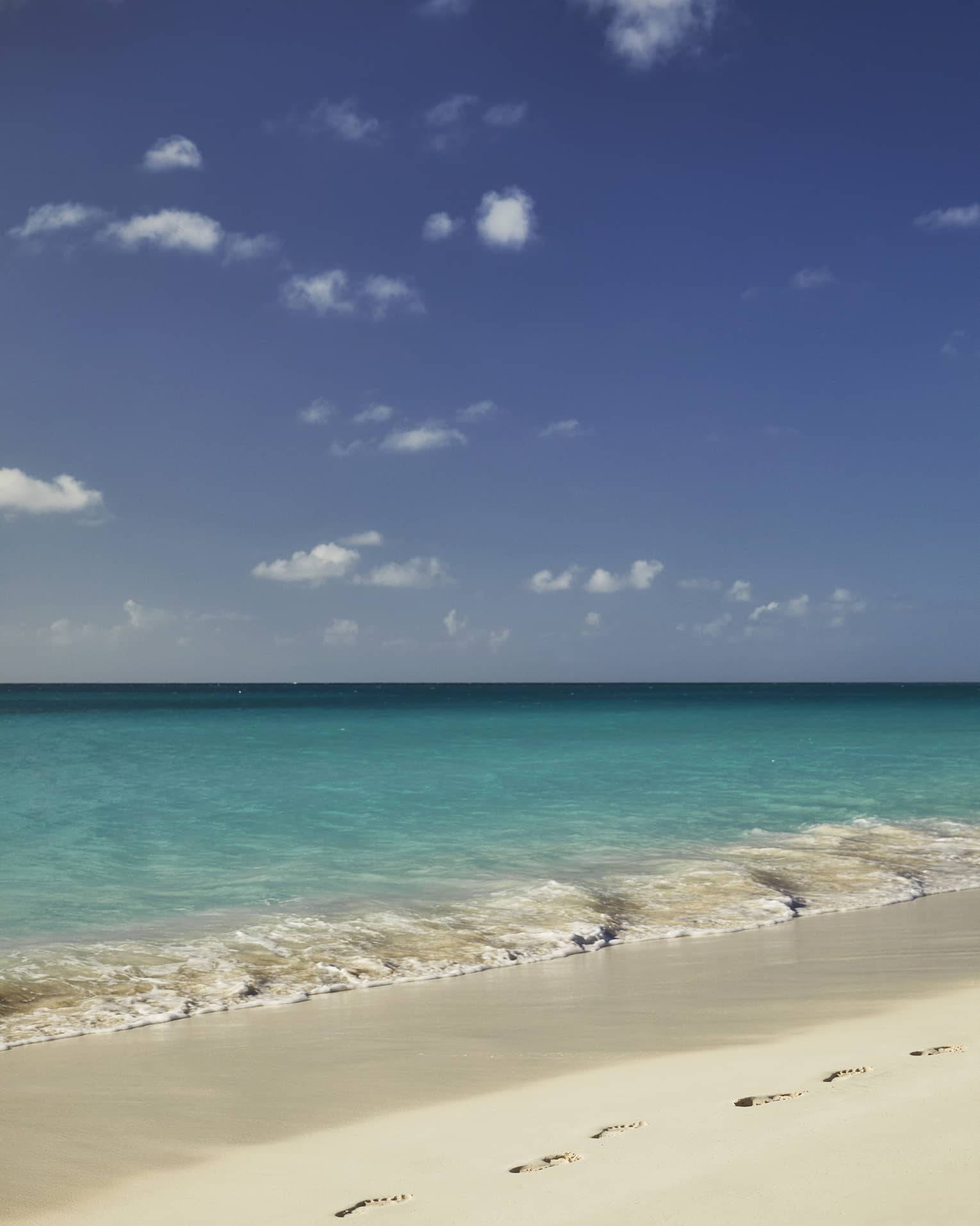 A sublime beachside view of endless turquoise ocean under blue sky dotted with wispy clouds, gentle waves lapping white sand.