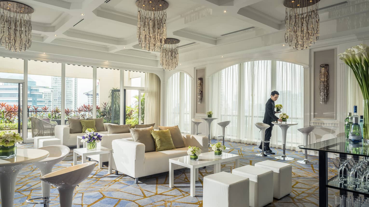A bright room is decorated with plush couches, tables with flowers and artistic chandeliers