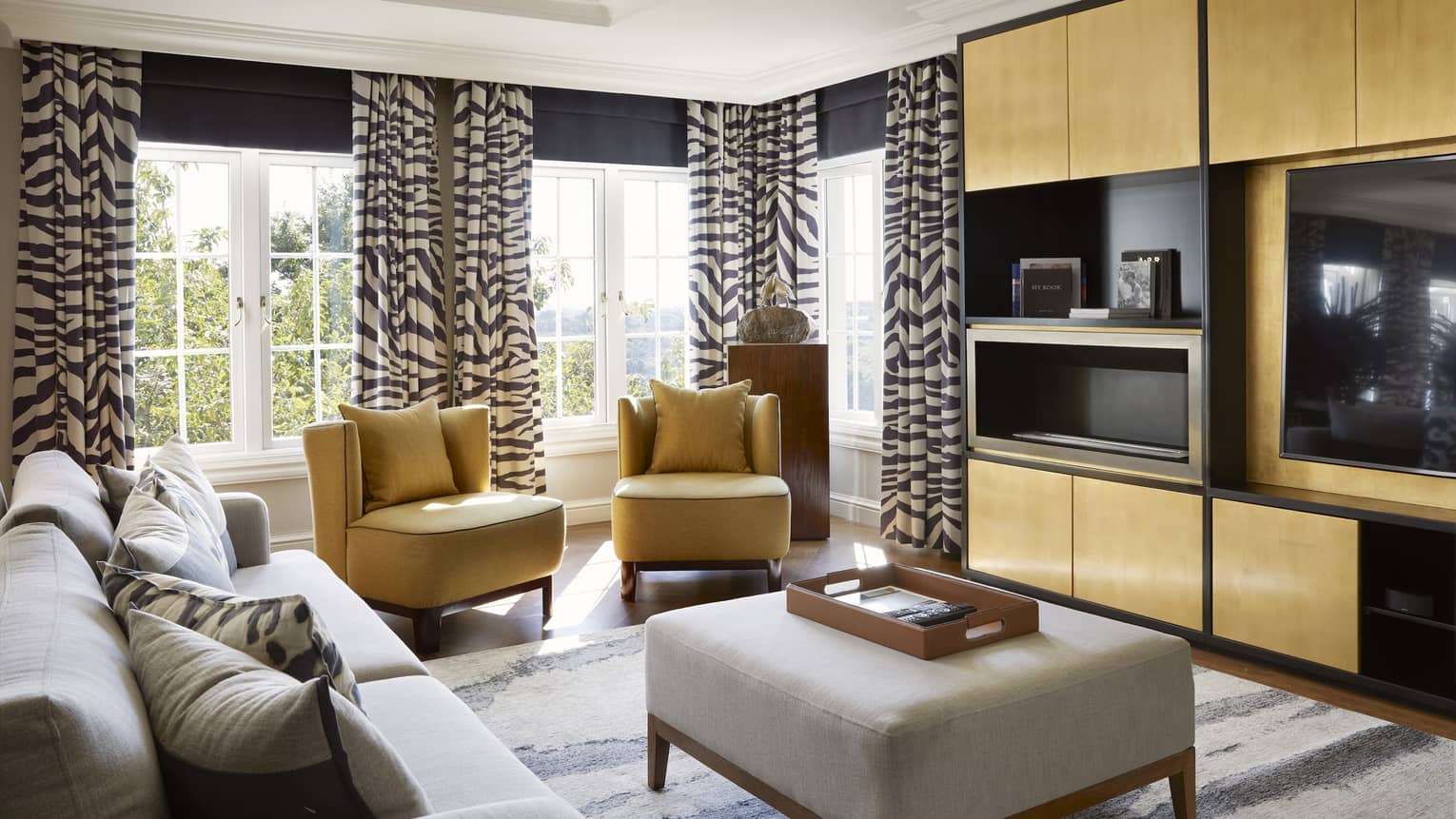 Luxury hotel suite living room with modern, light grey sofa, two yellow arm chairs, media centre and zebra-patterned curtains, at Four Seasons Hotel Johannesburg