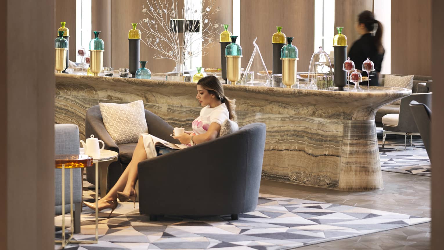 Woman drinks tea in large armchair by marble buffet bar