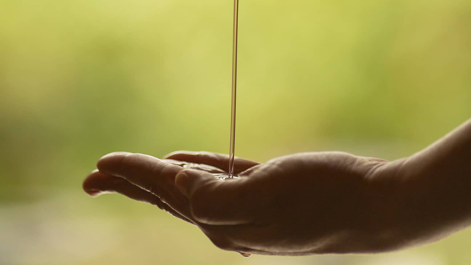 A set of hands pours massage oil from a ceramic bowl into a palm