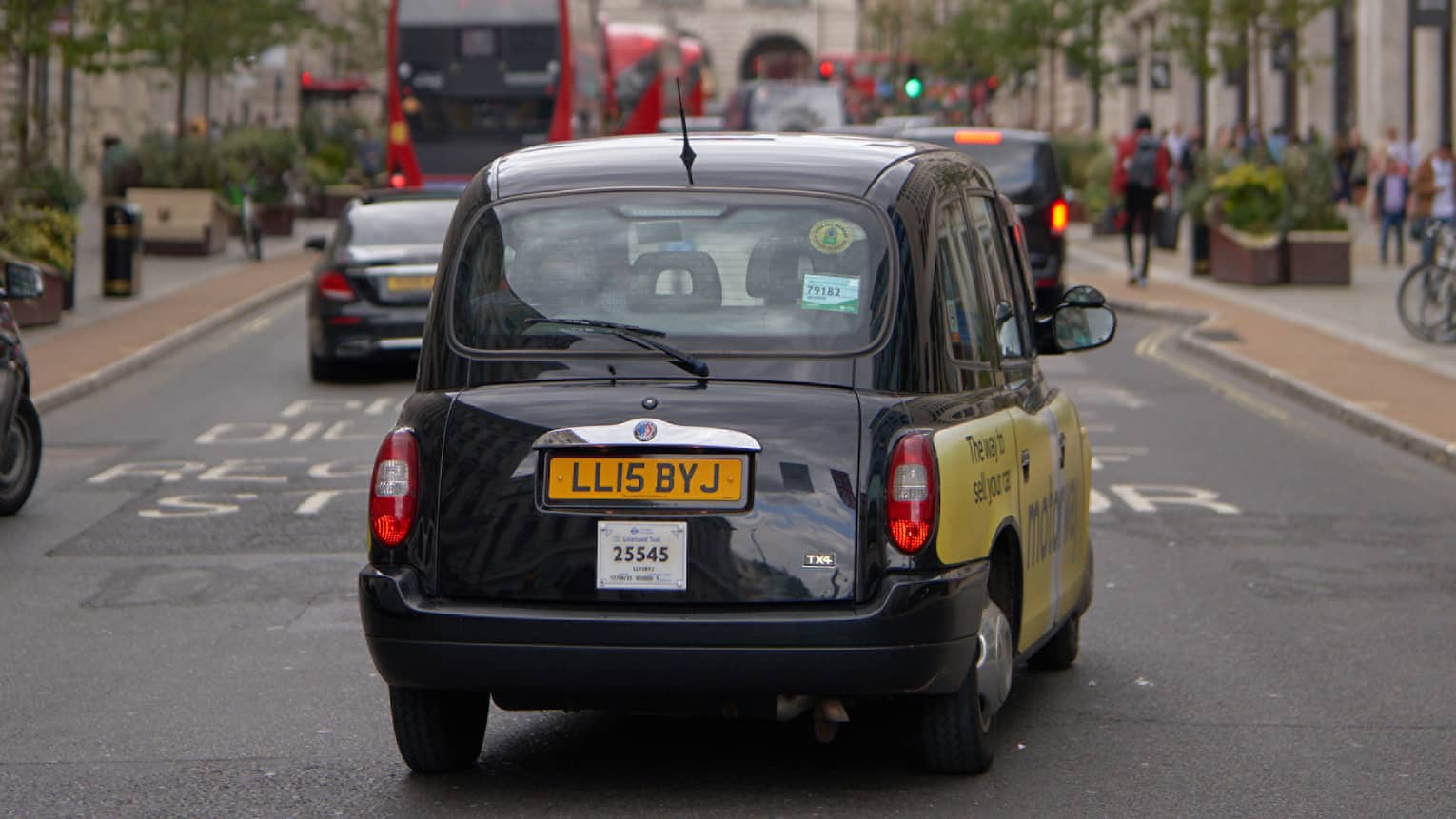 Rear view of London-style black cab, double-decker buses and other cars on road strung across with rows of Union Jack flags.