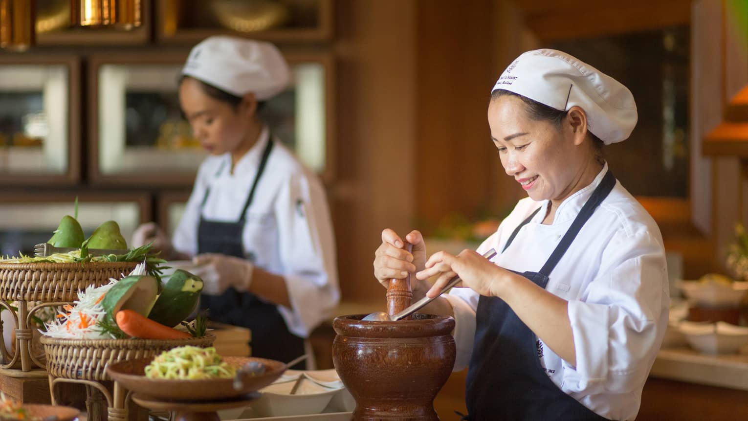 Two chefs in uniform prepare authentic Thai cuisine dishes at counter with fresh vegetables