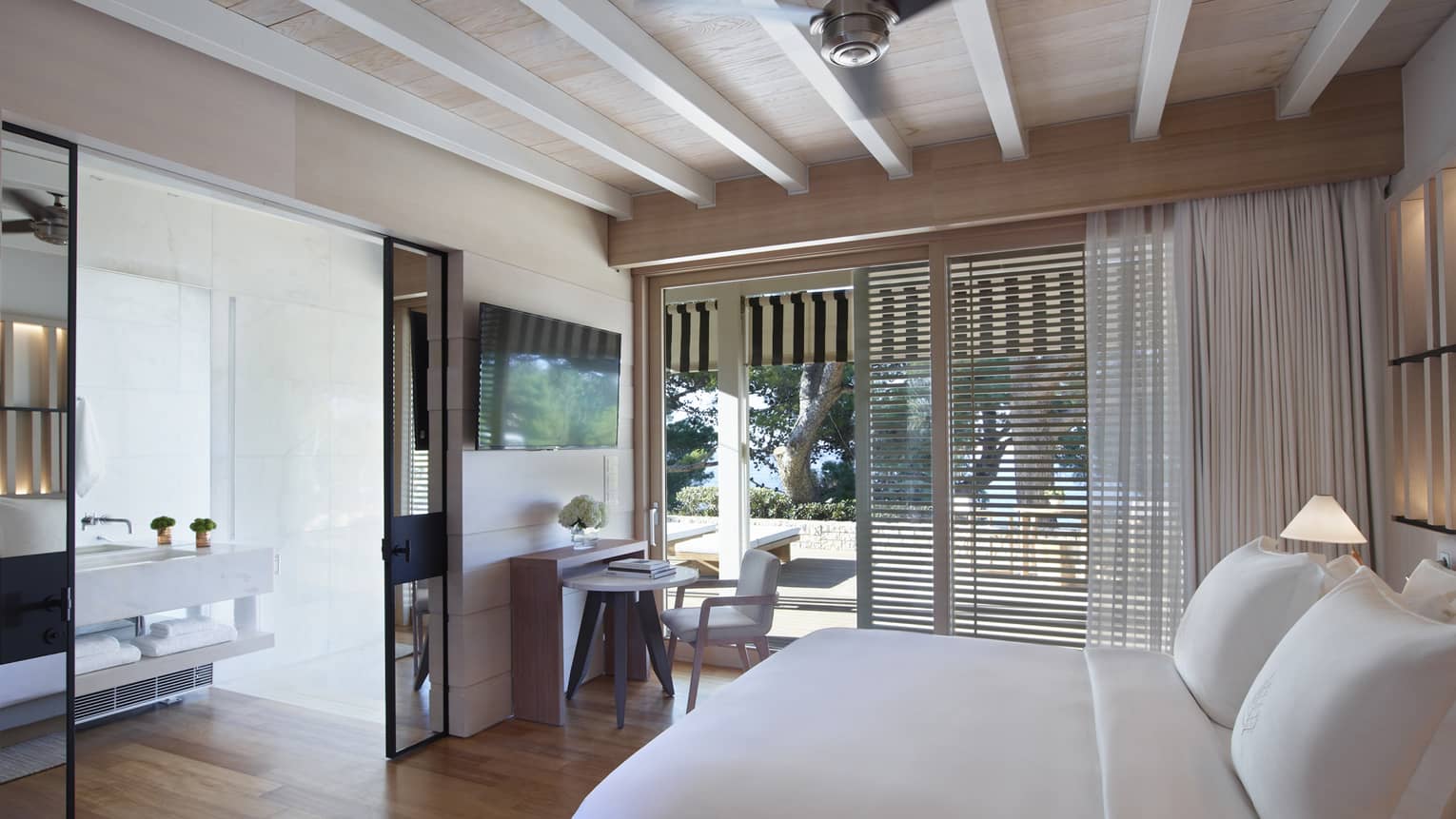 Guest room with white king bed, exposed rafter ceiling, sliding doors opening onto patio, mirrored doors to bathroom