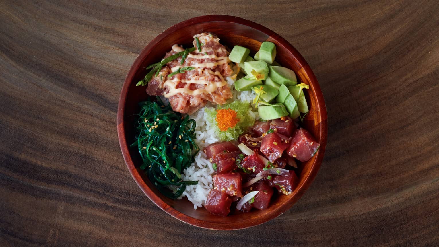 A bowl of poke, the Maui delicacy, stacked with raw fish, avocado, wasabi and greens, all perched on top of a bed of white rice