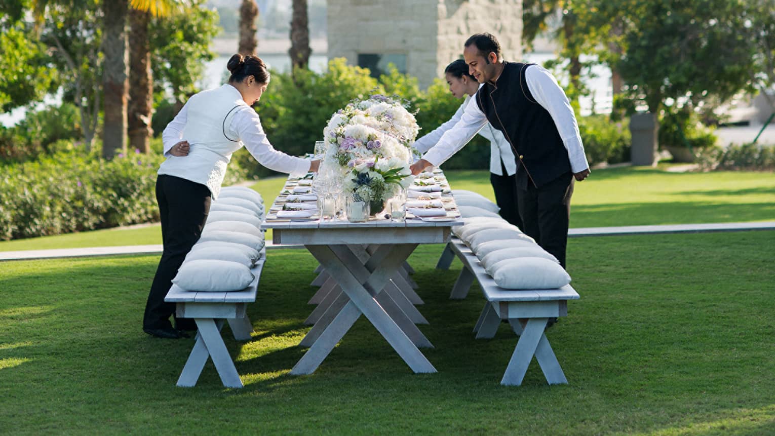 Hotel staff set outdoor wedding dining table on event lawn