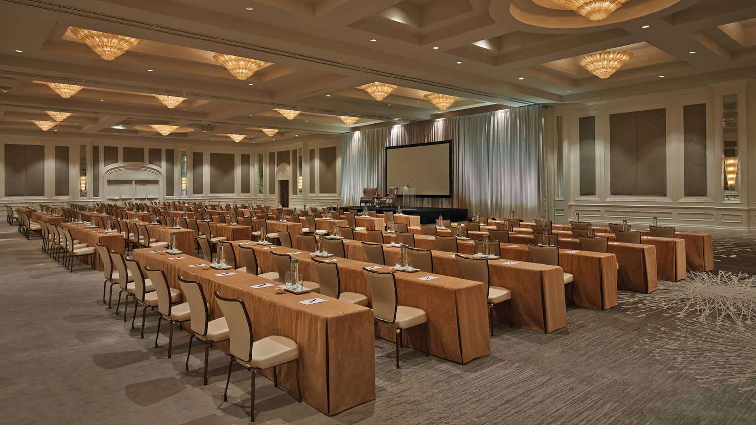 Conference with rows of meeting tables, chairs under cone-shaped lights in large ballroom