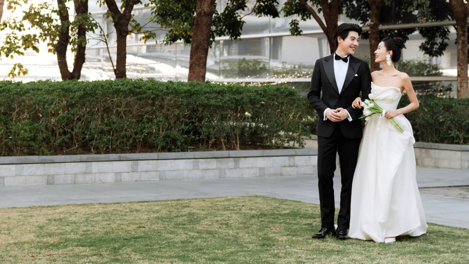 Bride and groom stand on outdoor terrace flanked by trees