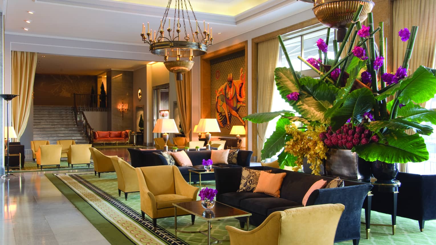 Sunny hotel lobby with blue sofas, yellow armchairs, large tropical plant with purple flowers