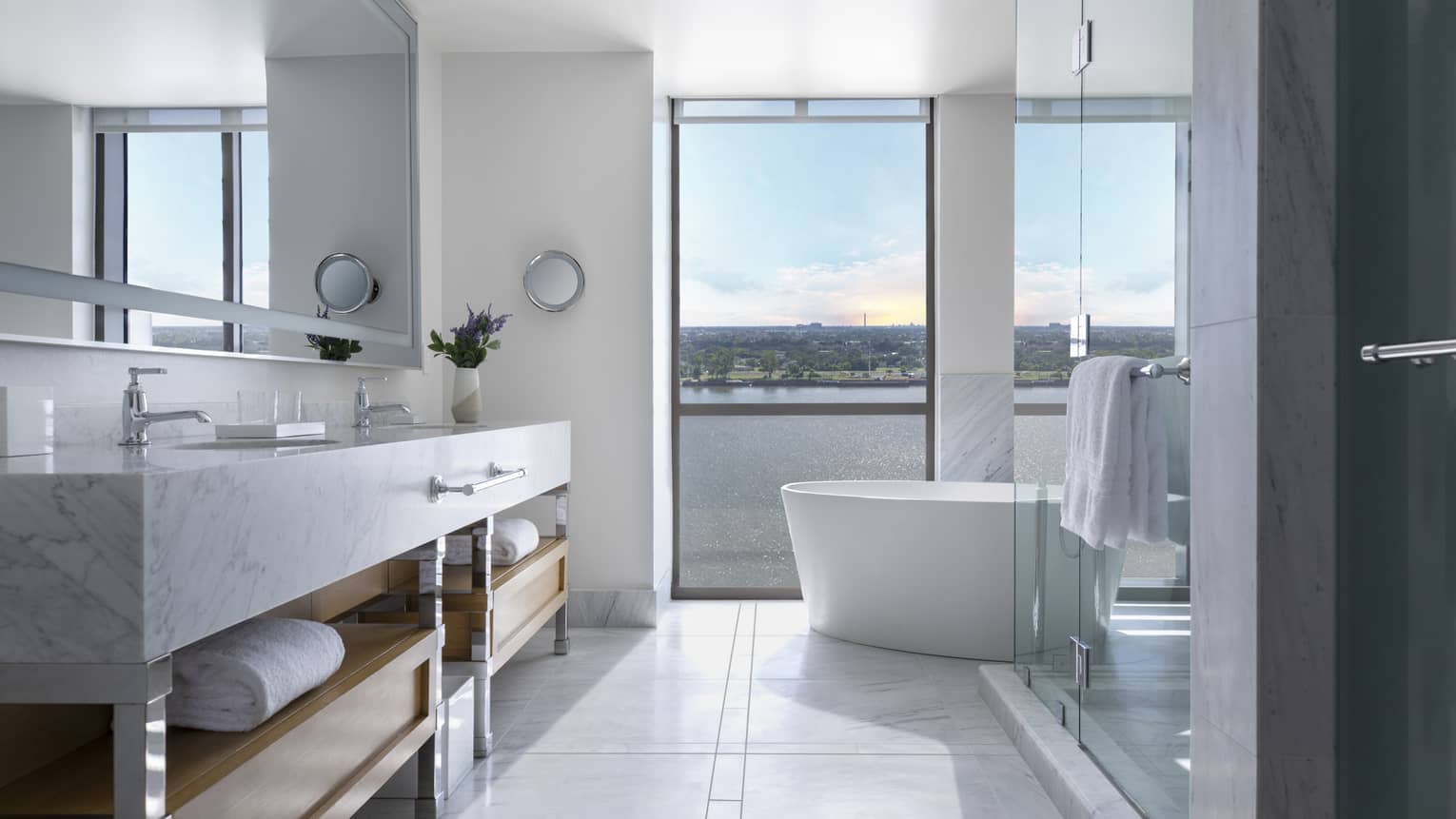 Guest room bathroom with marbled double vanity, full-width mirror, large soaking tub, floor-to-ceiling window