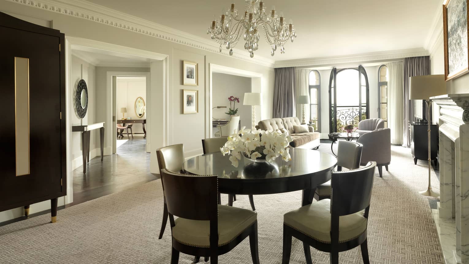 One-bedroom Suite round dining room table for 6, small crystal chandelier, living room, French doors to balcony in background