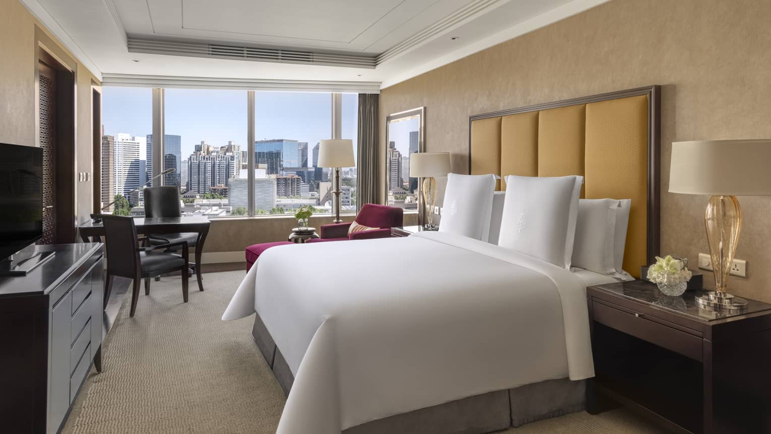 Hotel room with king bed, tan headboard, desk with two chairs, dresser and window-side chaise