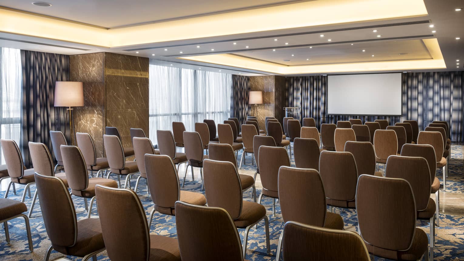 Rows of chairs facing screen in large meeting room with marble pillars