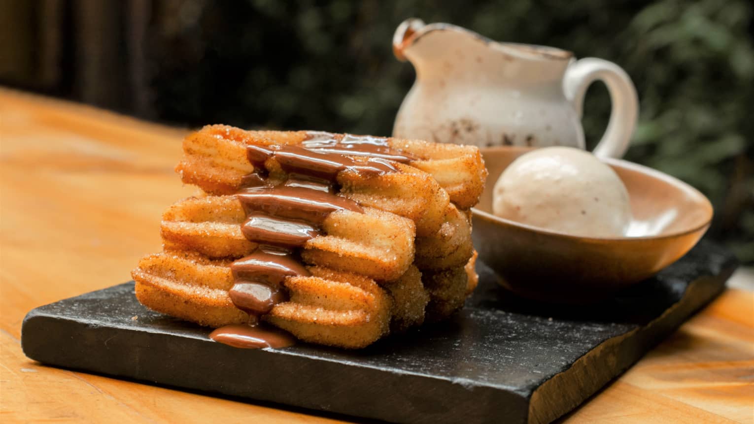 Pastries with chocolate on a black tray with ice cream in a bowl.