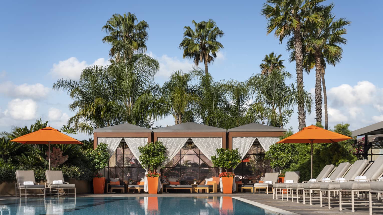 Outdoor pool with lounge chairs, umbrellas and cabanas.