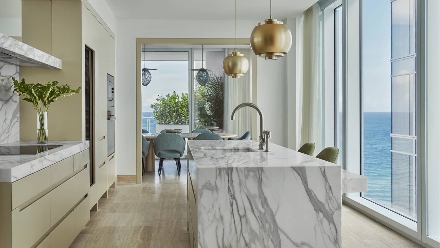 Retro-style brass lamps above grey marble kitchen island, glass wall with ocean views