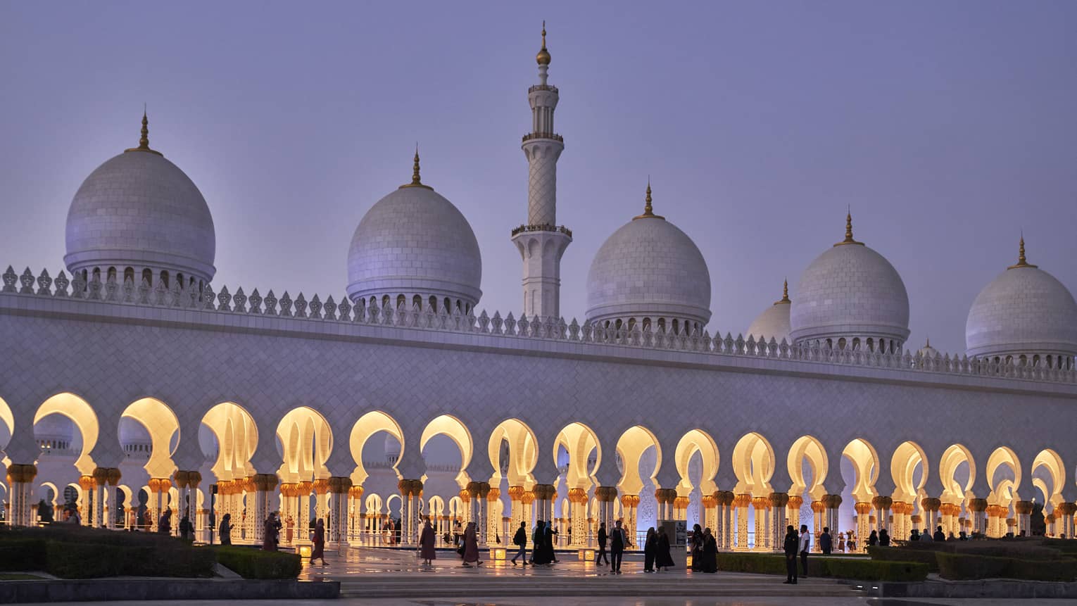 Stunning white marble mosque at dusk features a minaret with pointed domes at either side; keyhole arches line the entrance.