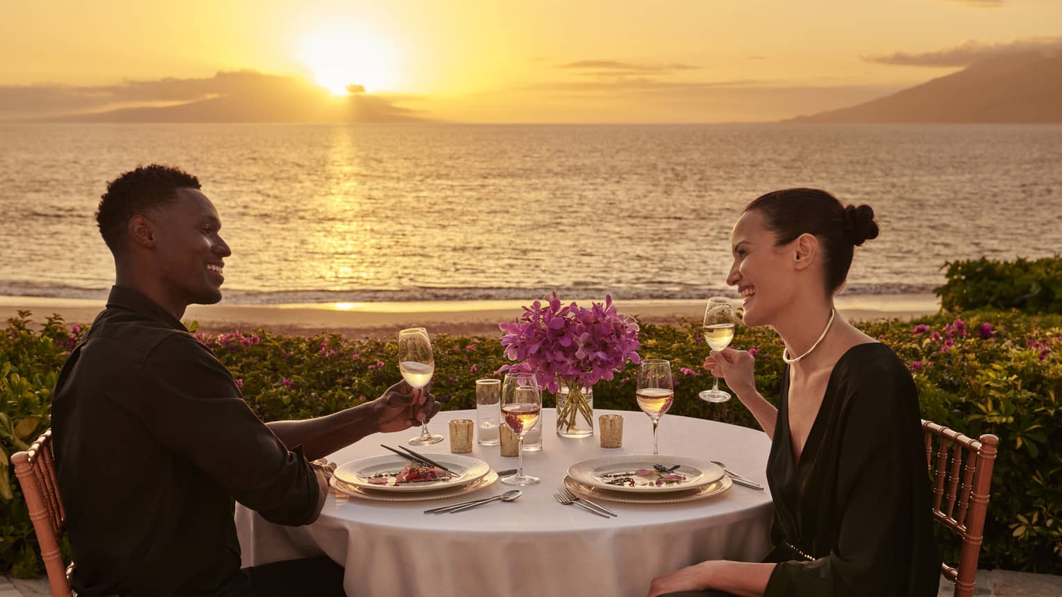 Man and woman at romantic dinner table with sunset and ocean view