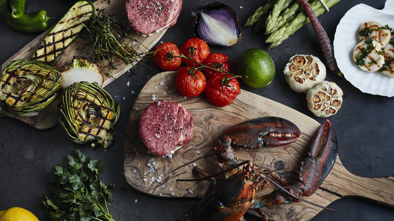 Brasserie grilled lobster, artichoke halves, whole tomatoes on wood chopping board 