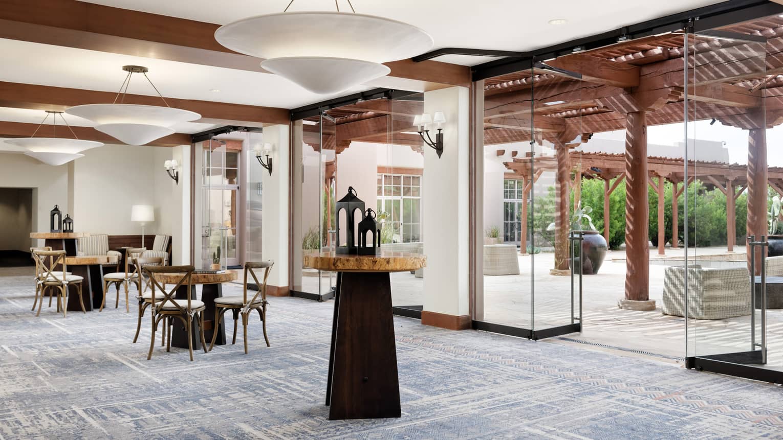 A foyer/seating area with small tables and wooden chairs, glass doors and windows cover the wall.