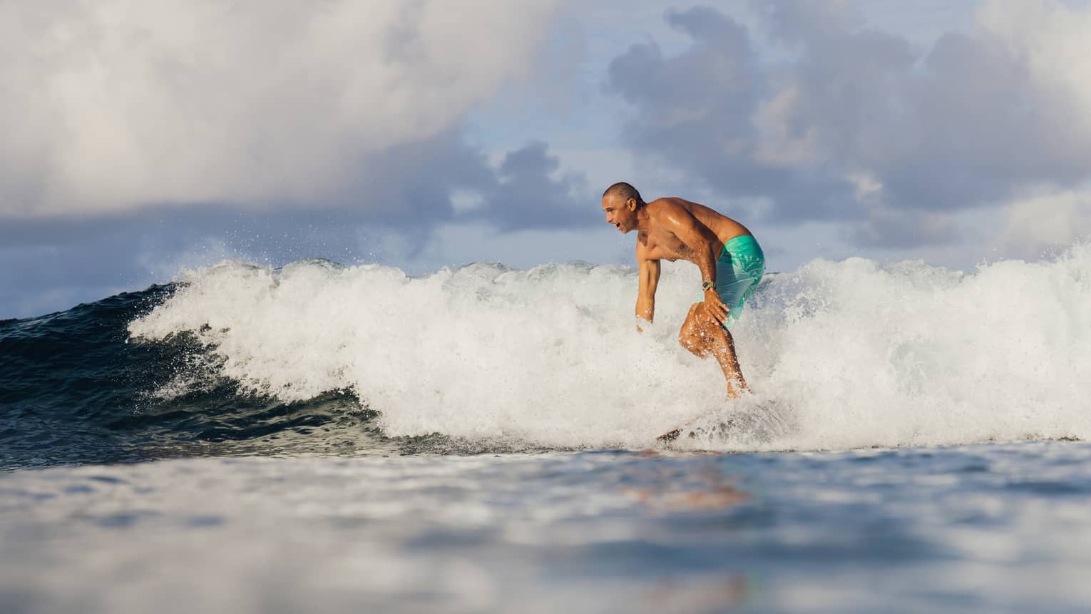 Surfboard designer Bonga Perkins in teal board shorts crests a wave
