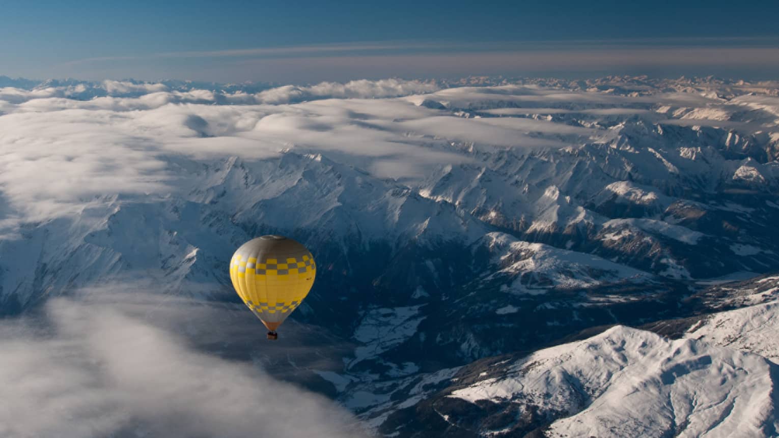 Yellow hot air balloon soaring over the snow-covered Alps