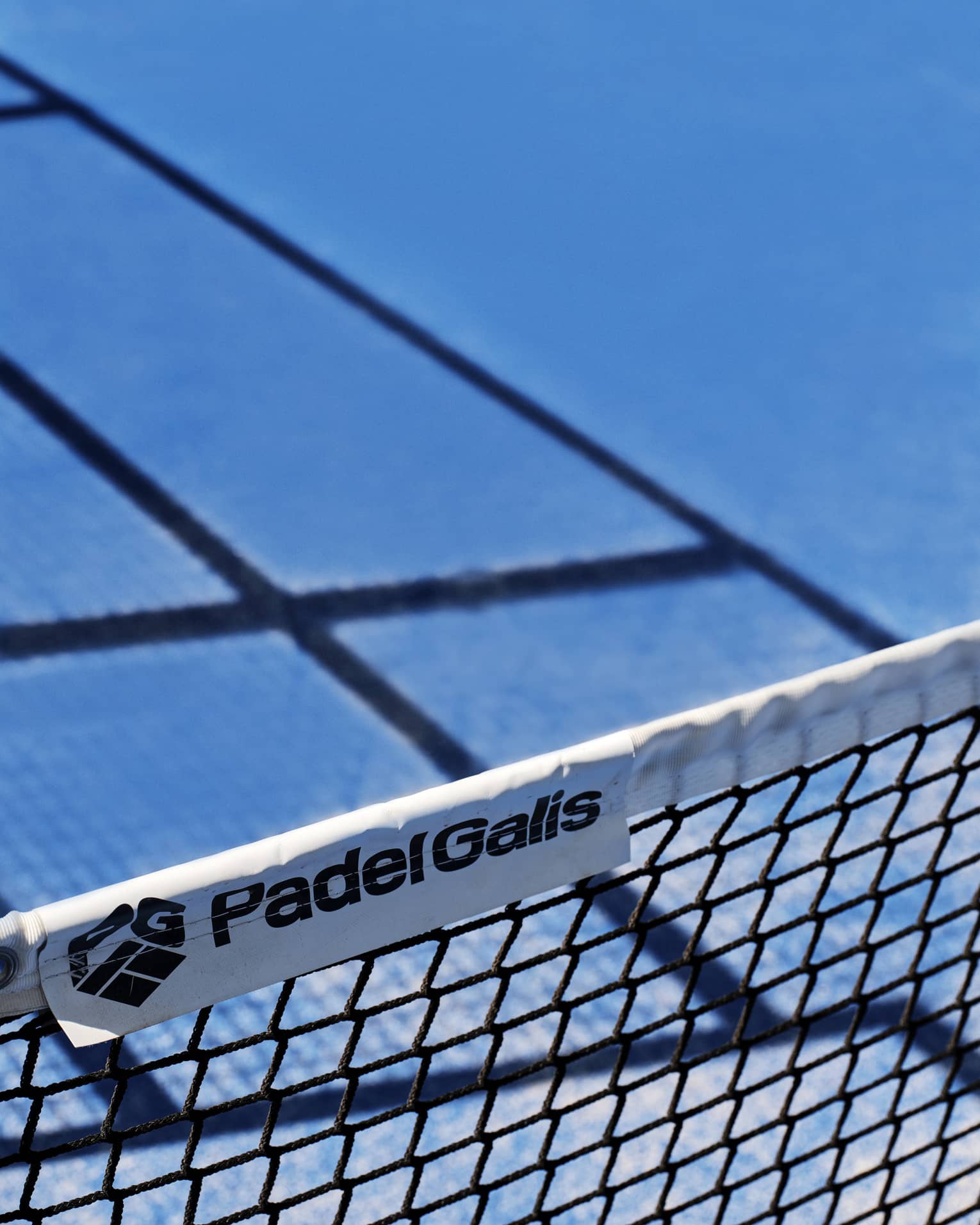 A close-up of the words, Padel Galis, and the company logo on a label of a net on a tennis court.