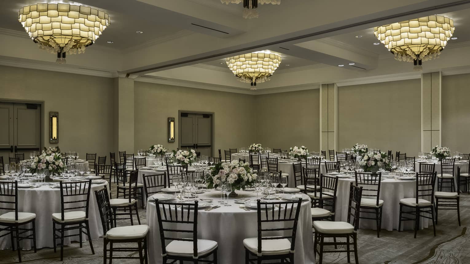 Large round banquet dining tables and chairs under three small chandeliers