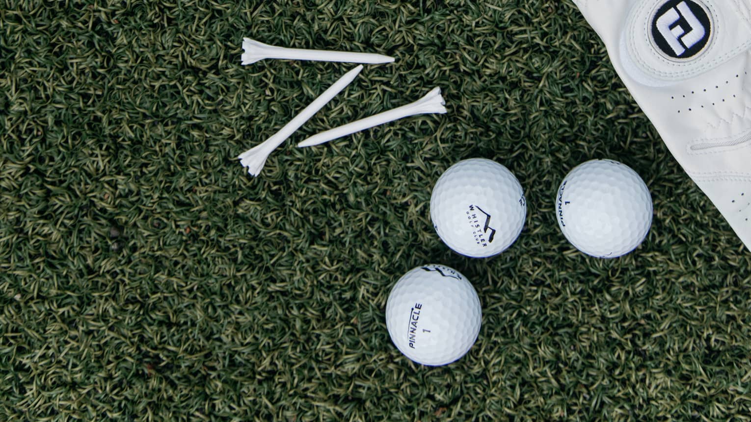 On green turf, a Four Seasons card, three golf balls, three tees and a white leather golf glove dotted with tiny holes.