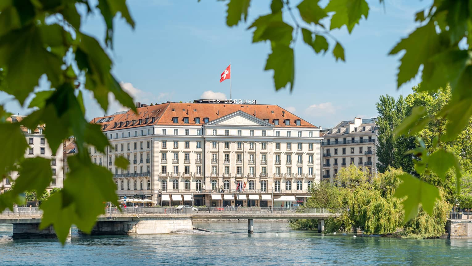 Four Seasons Hotel Geneva surrounded by green foliage, Lake Geneva in the foreground