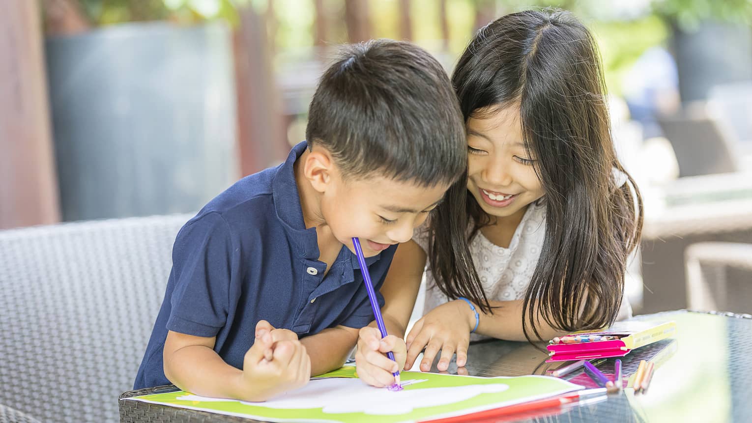 Smiling young boy and girl colouring in book with crayon