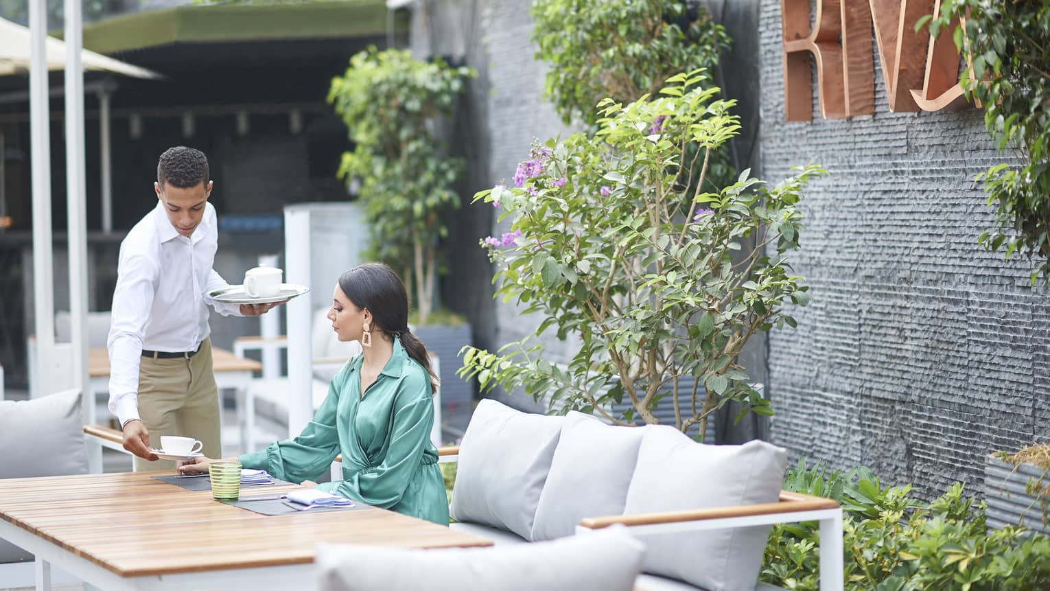 Woman in green dress seated at Riva restaurant terrace table, being served afternoon tea