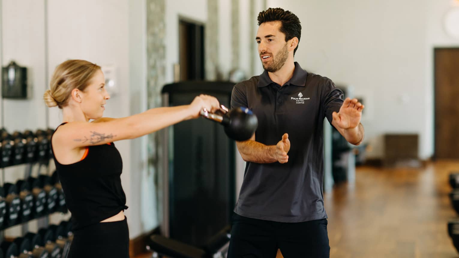 Male fitness trainer works with female guest who is using a kettlebell