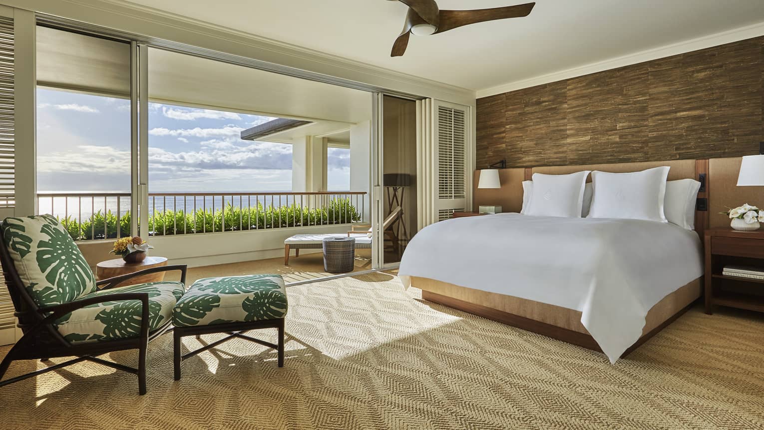Hotel room bed and tropical print armchair by open air wall to patio, ocean view