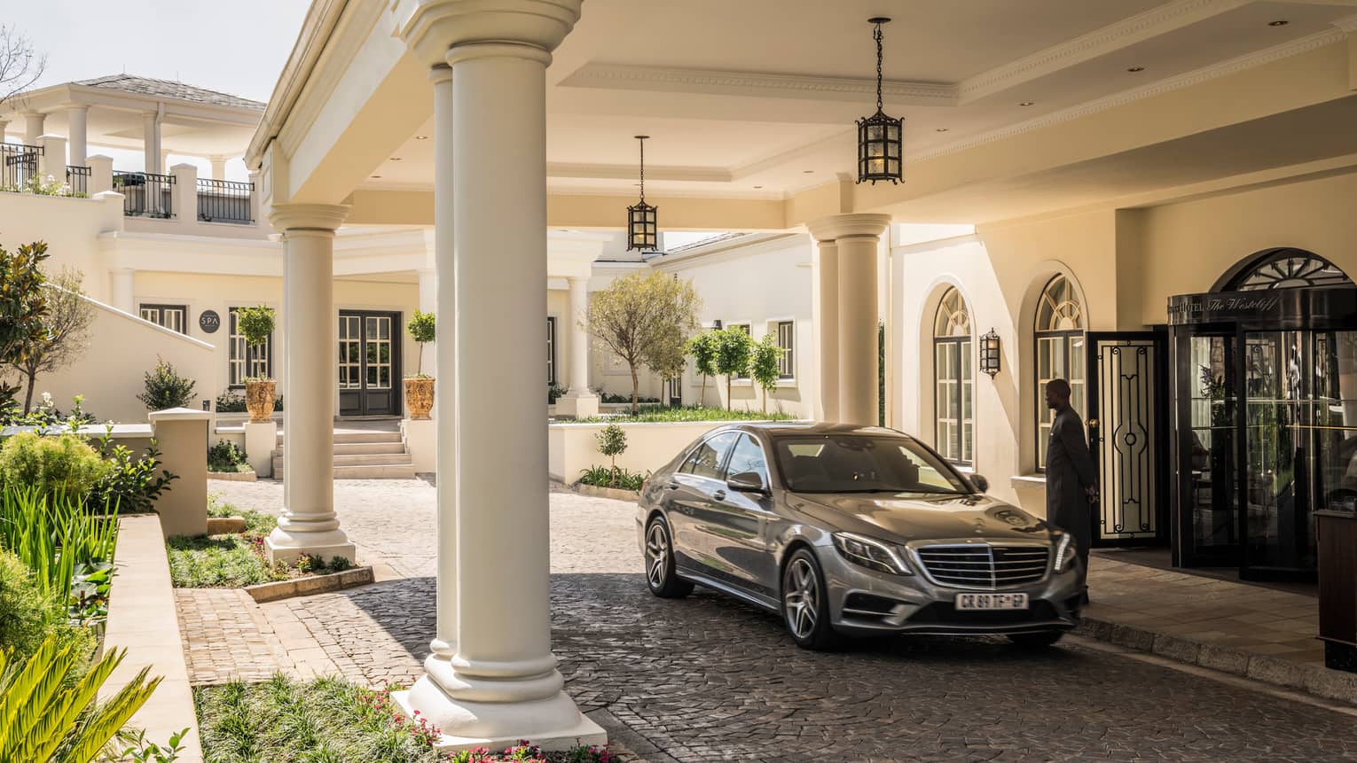 Man greets luxury car under white pillars at front entrance to Four Seasons Hotel The Westcliff, Johannesburg