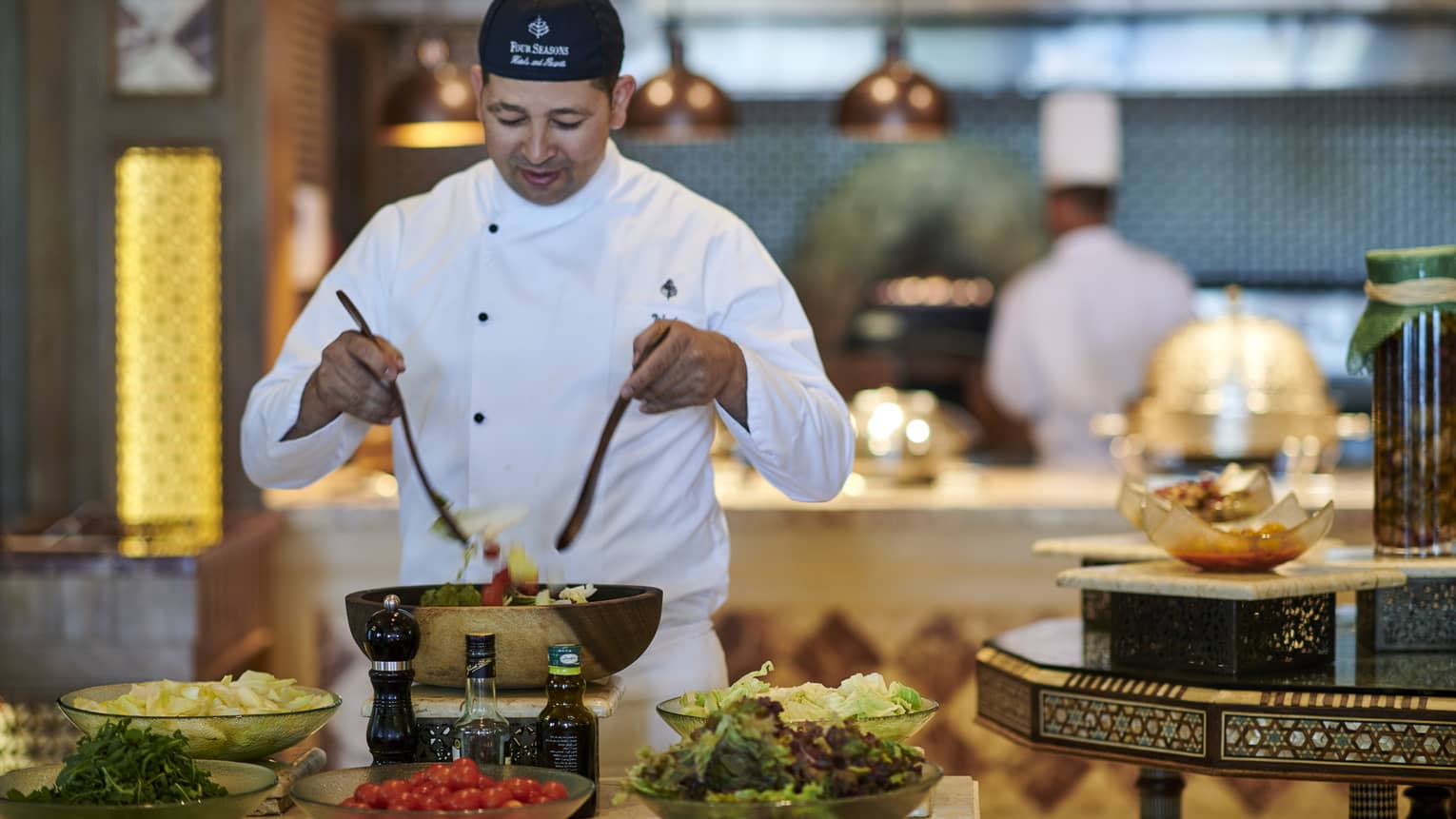 Chef tosses salad at buffet station with chopped vegetables in bowls